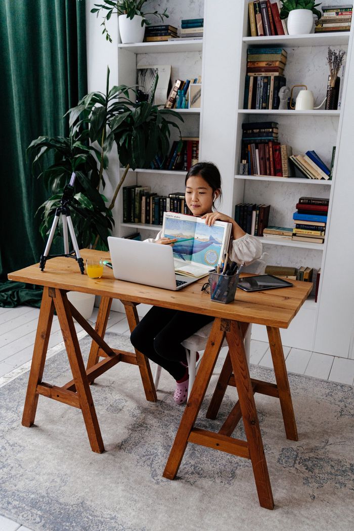A young girl engaged in online learning at home, sitting at a desk with her laptop and books.